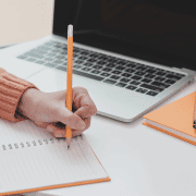 Studierende macht Notizen in ihrem Planer, die Ihr beim Verfassen ihrer Hausarbeit helfen. Neben ihr steht ihr Laptop.